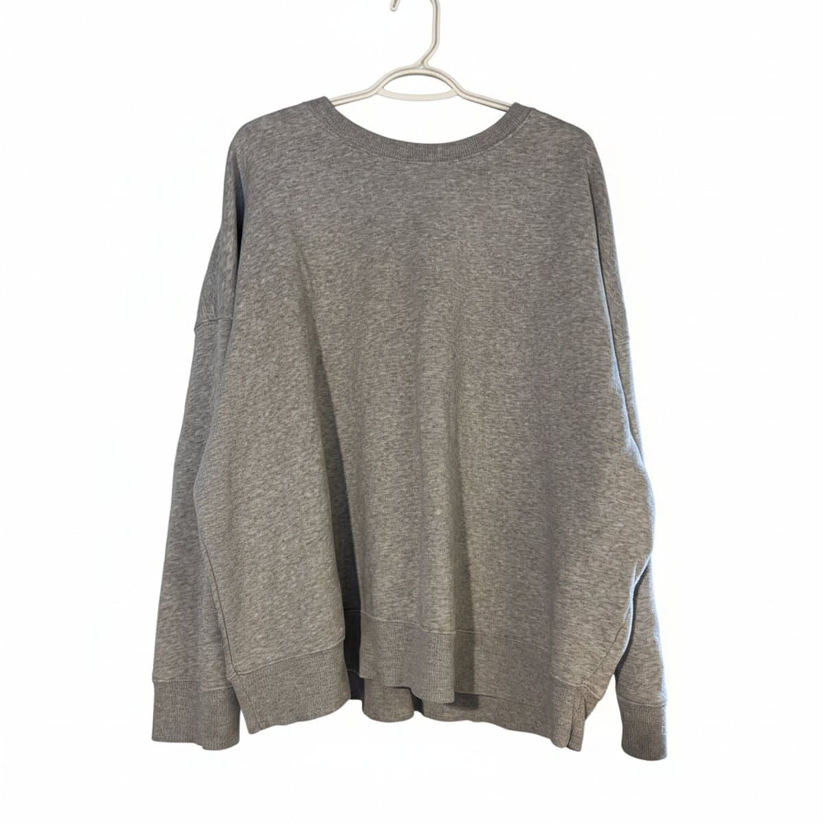 A classic heather grey relaxed fit crewneck sweatshirt with ribbed cuffs, displayed on a hanger, available at handpicked306 boutique in Carlyle SK.